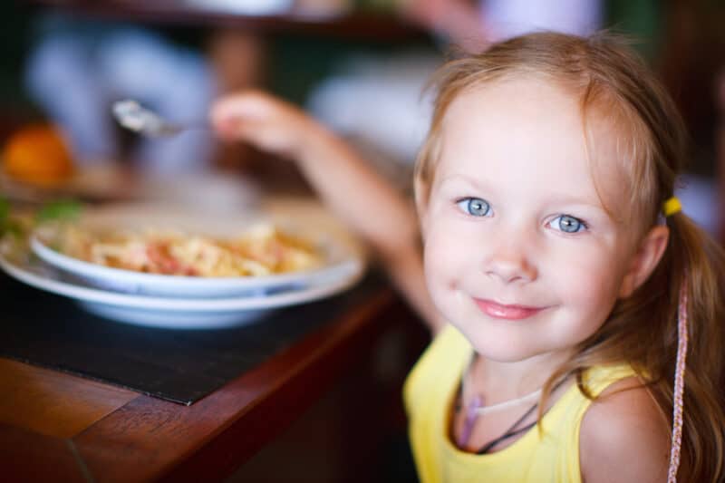 Portrait of a young girl eating at a table and smiling.